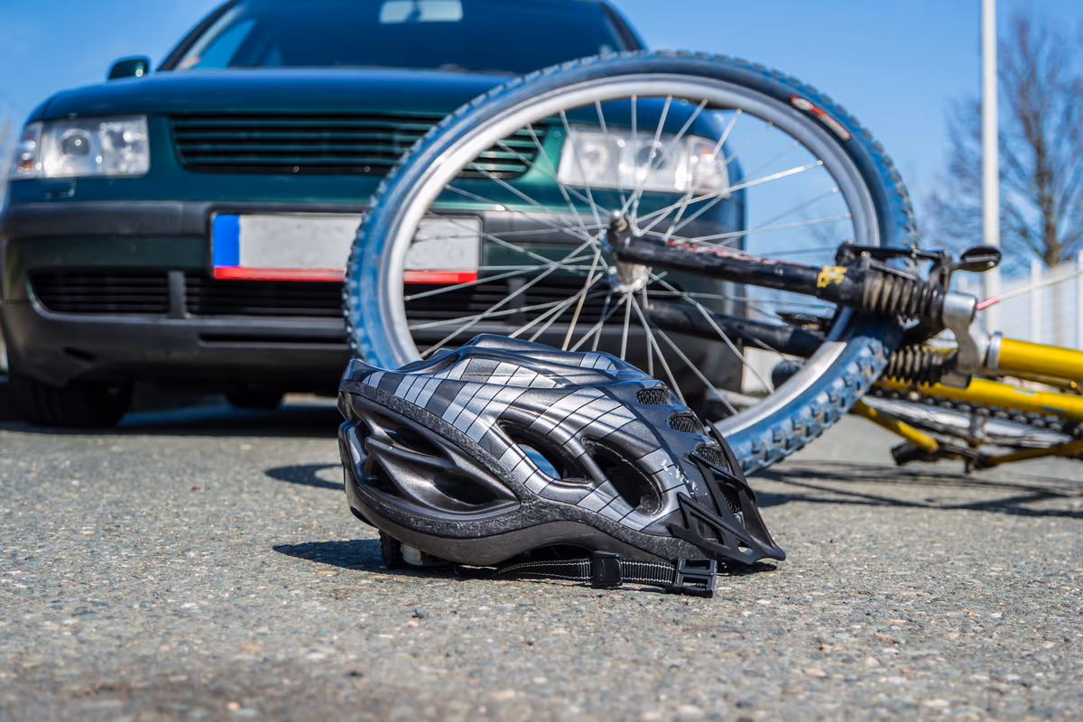 A bicycle and helmet on the road beside a car after a collision